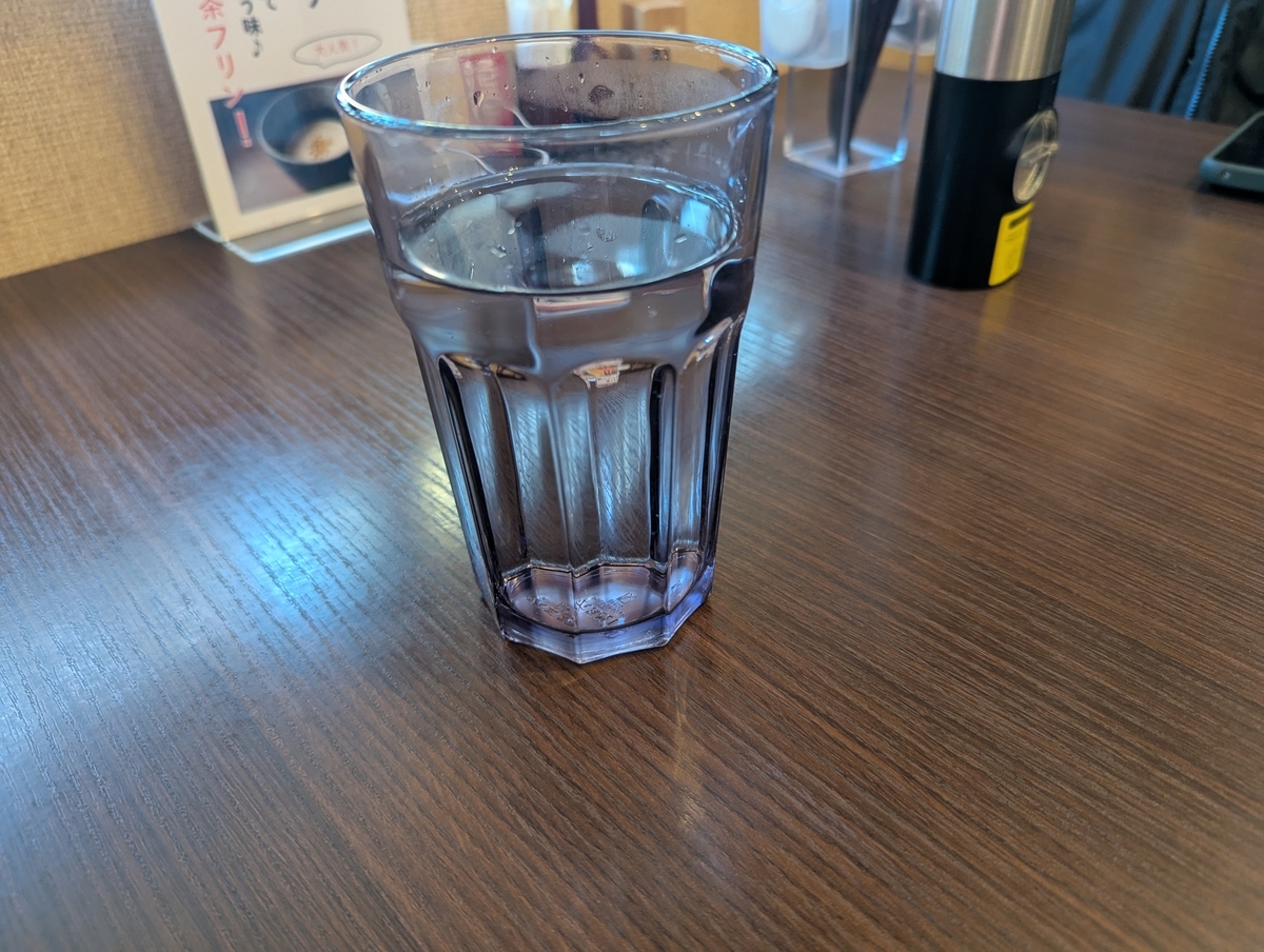 立川たかやで最初に提供される白湯。木目のテーブルにグラス一杯の白湯が置かれている