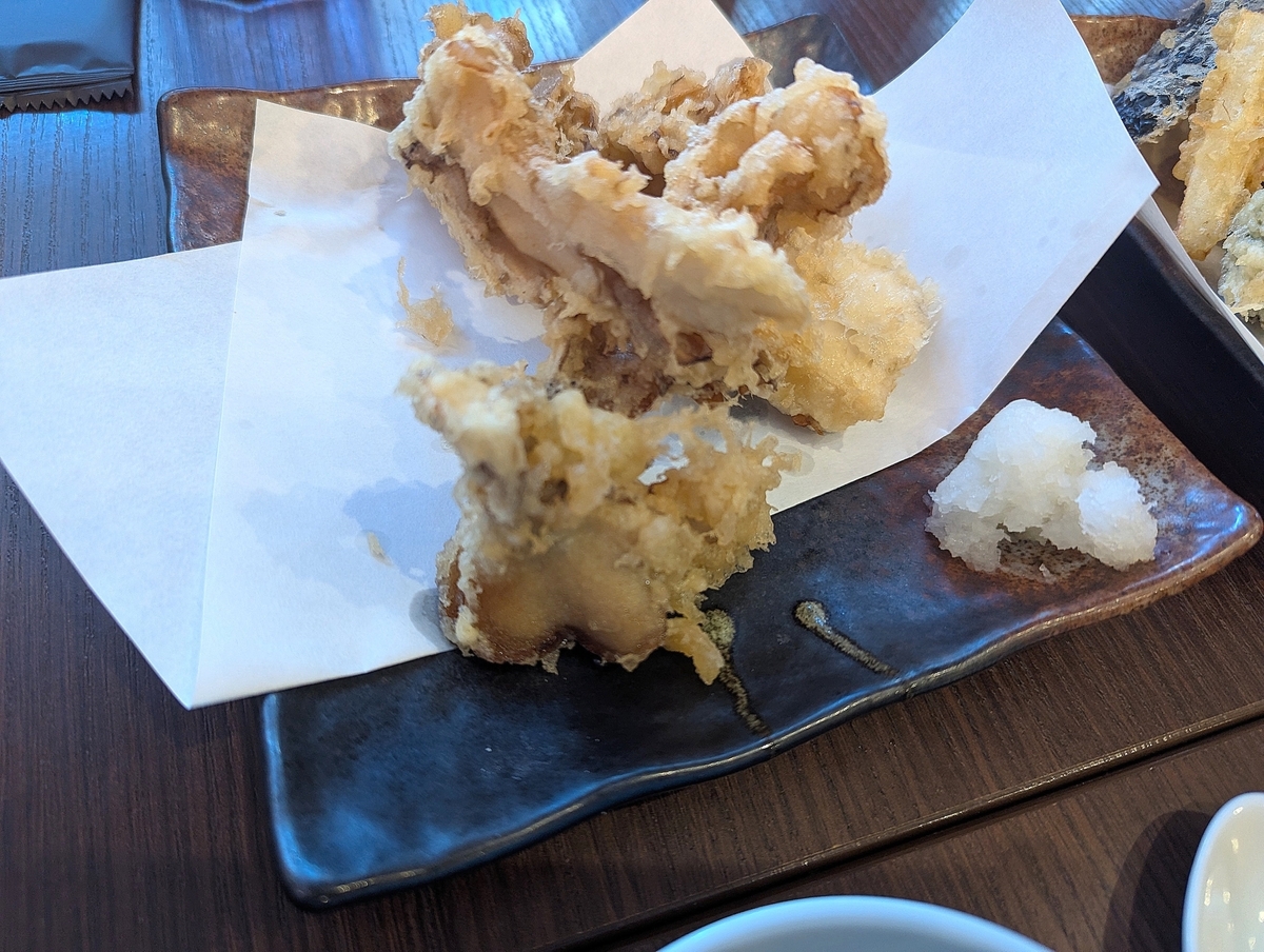 立川たかやの雪国舞茸天ぷら。黒い長皿に敷紙を敷き、肉厚な舞茸の天ぷらが二房盛られ、添えに大根おろし