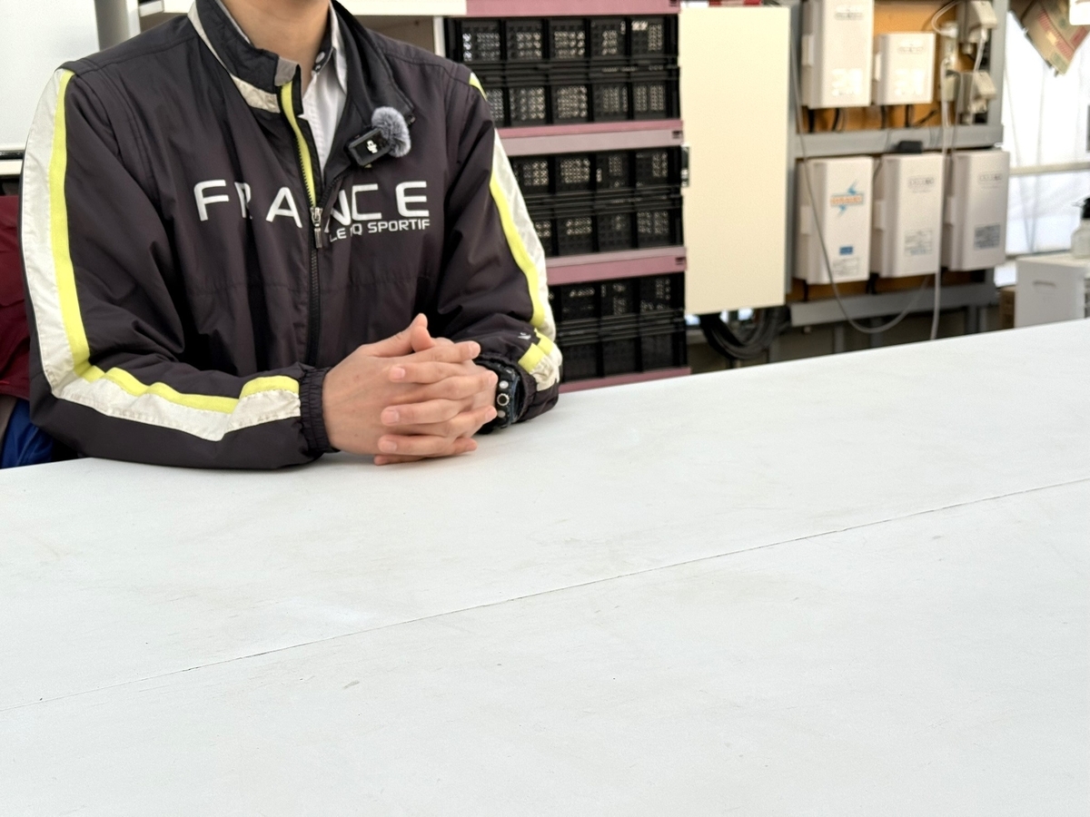 澤藤園代表・澤井政善氏へのインタビュー風景。フランス代表モデルのジャケットを着て両手を組み、白いテーブルでこちらに向かって話している(顔は写さず)