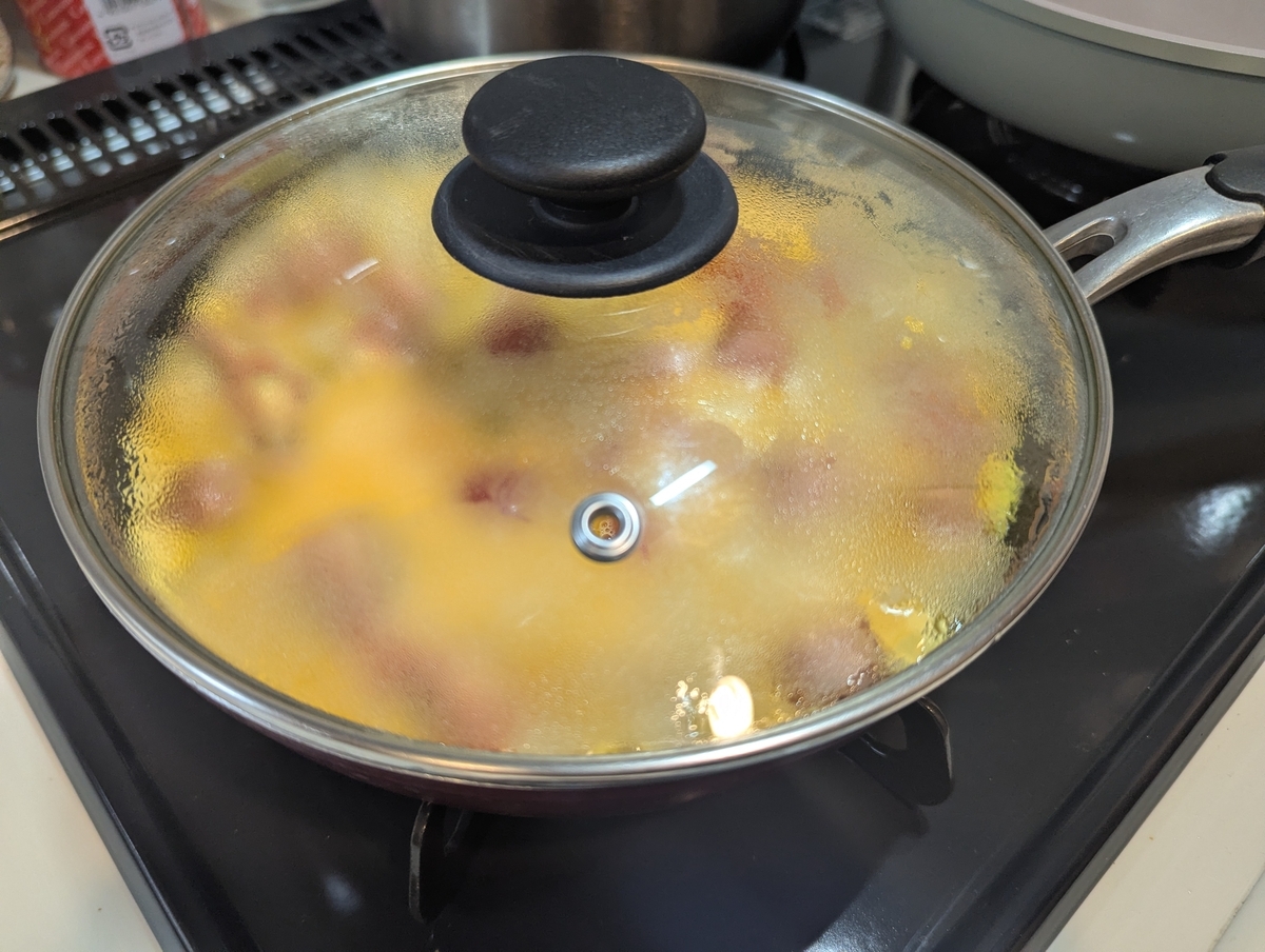 ガラス蓋に湯気が立ち込めるフライパン。中ではスパニッシュオムレツが蒸し焼き状態で火が通っている様子が透けて見える