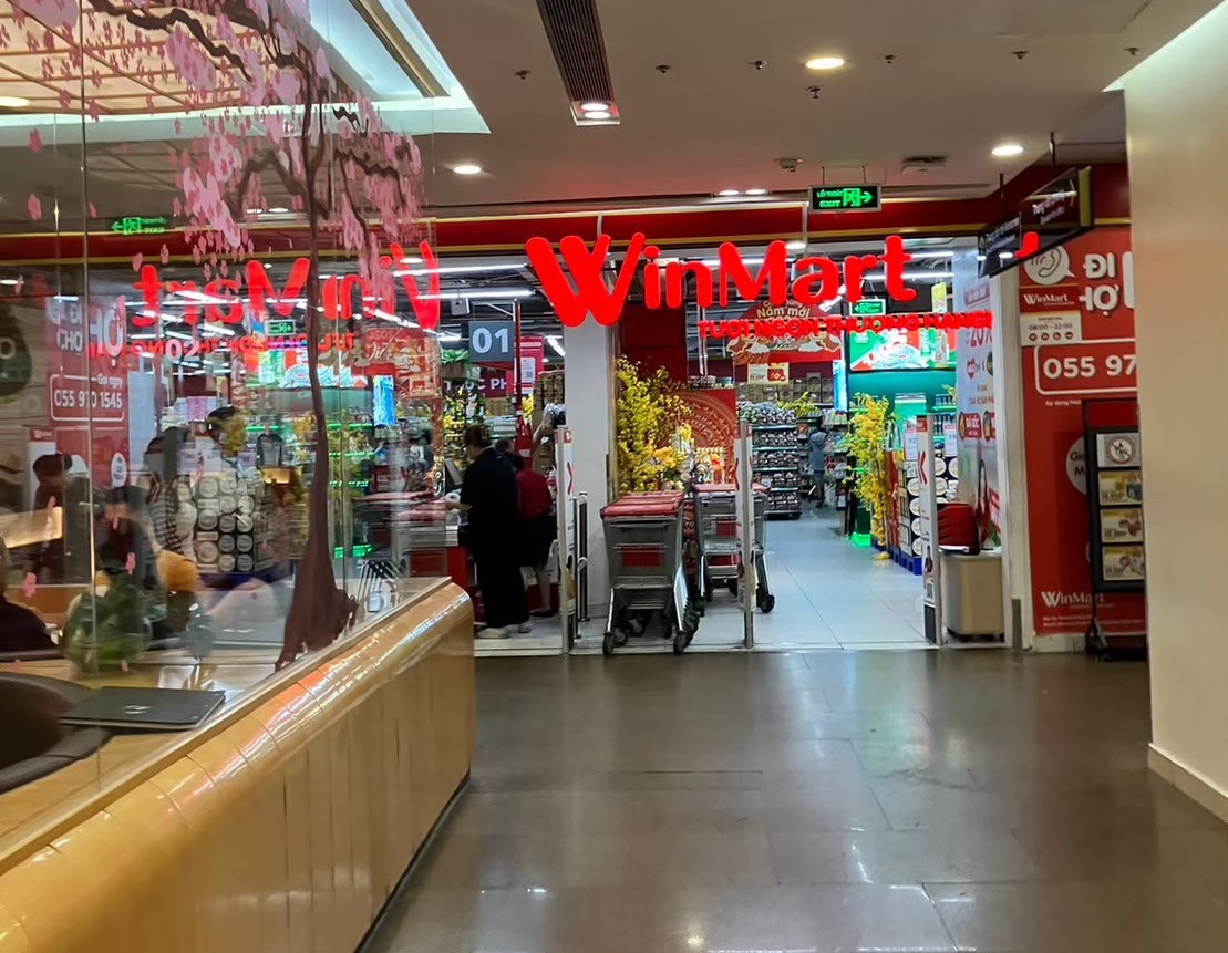 ホーチミンのショッピングモール内にあるベトナム最大級のスーパーチェーンWinMart店舗入り口。テト（旧正月）の桜・黄色い菊・赤い装飾が華やかに飾られ、新年のショッピング客で賑わっている