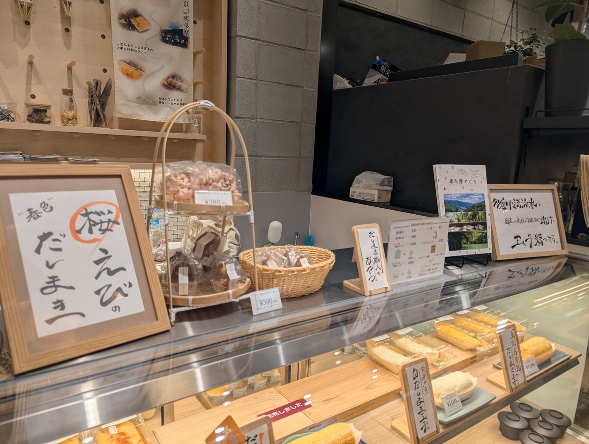 卵道 エキュート立川店の店頭ディスプレイ。春色 桜えびのだしまきの手書き札、東京・奥多摩のポスター、出汁素材瓶、奥多摩めぐりパンフレットが並ぶ