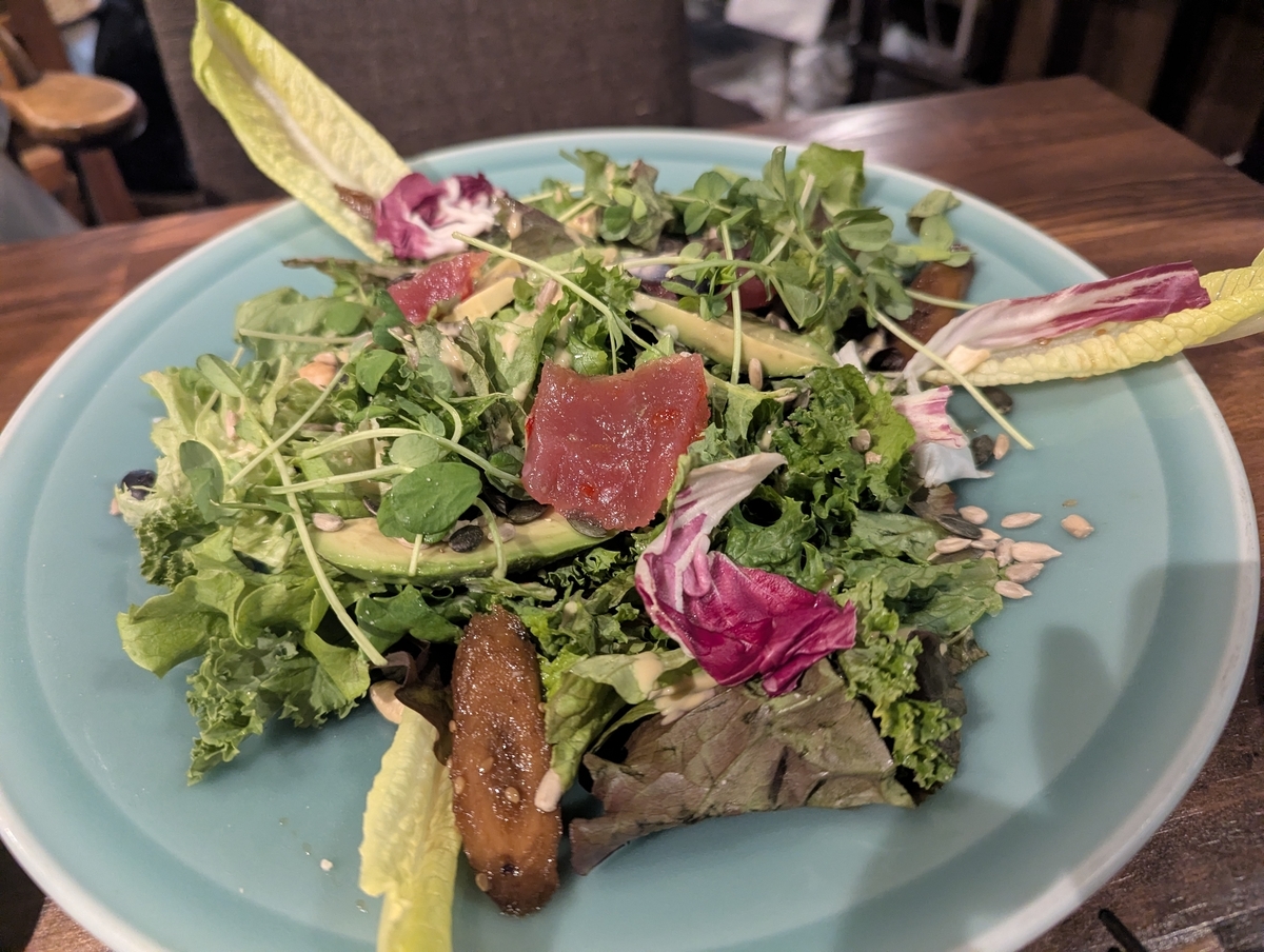 ターコイズブルーの皿に山盛りの葉物野菜、アボカド、マグロ、紫キャベツ、ベビーコーン、ナッツ、雑穀米が層になったスペシャルサラダ