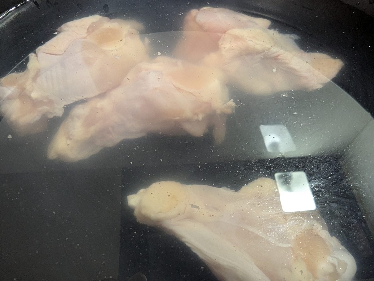 黒い鍋の中に水を張り、鶏もも肉を3〜4切れ並べた様子