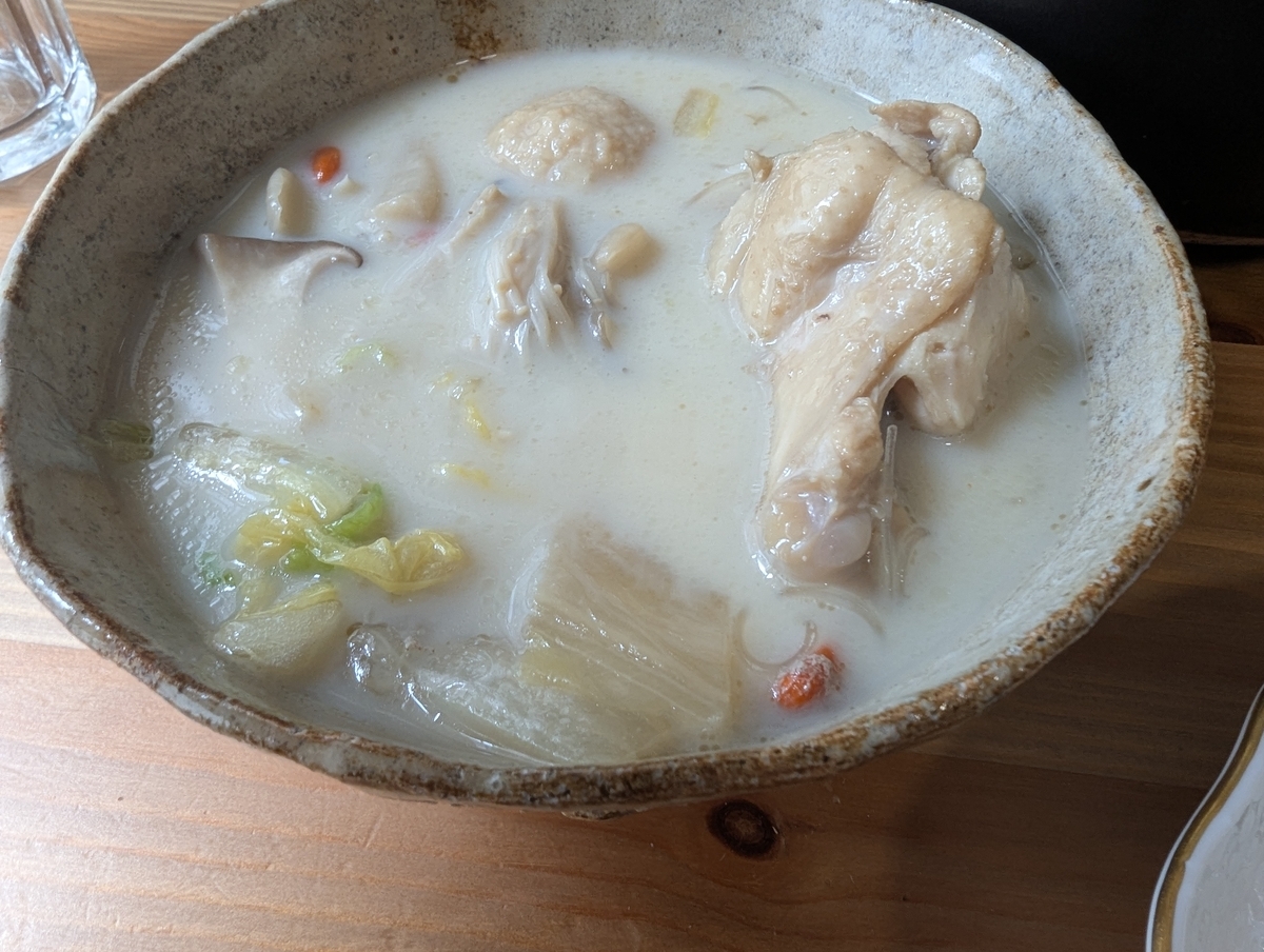 信楽風の素朴な器に盛られた、豆乳と練りごまを加えてクリーミーになった白濁スープの薬膳鍋。鶏もも肉、白菜、きのこ、クコの実が浮かぶ