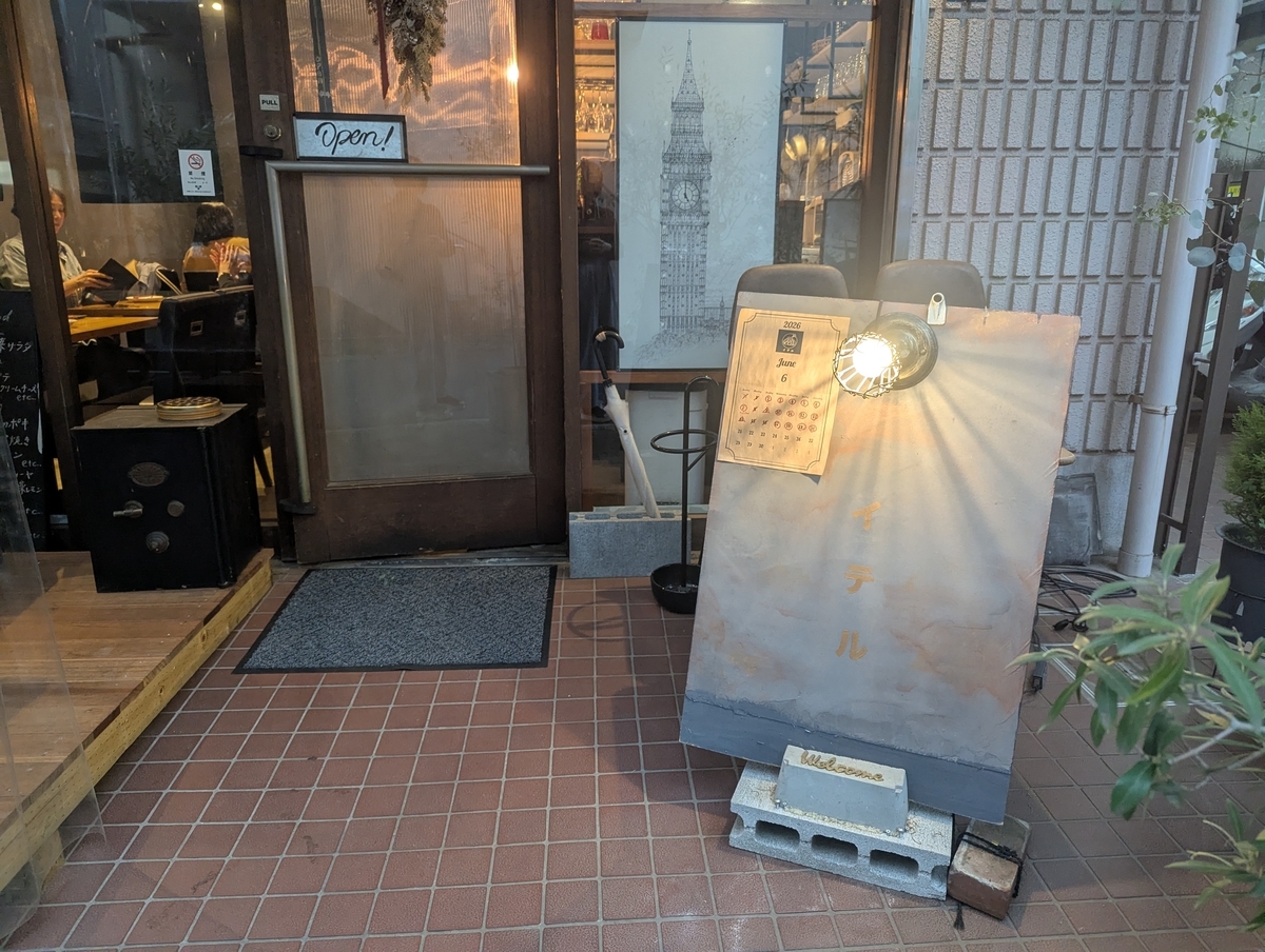 イテル-iter-の店頭。木製ドアにOpen!の札、「イテル」と記された手書き看板と6月のカレンダーが置かれた入口