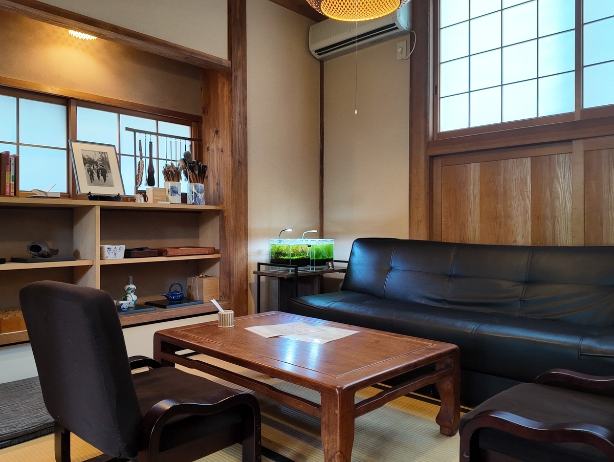 頑亭文庫の店内。畳の間に黒いソファとローテーブル、棚には筆や器が並ぶ