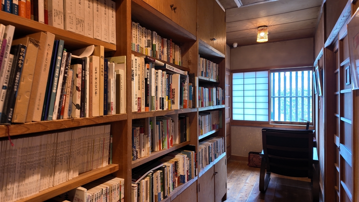 頑亭文庫の廊下一面に並ぶ蔵書と、奥のロッキングチェアの一人席