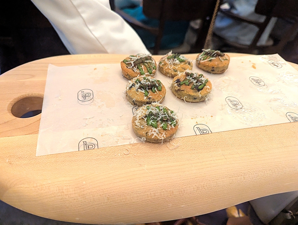 木のボードにのった丸い焼き地のフィンガーフード。アスパラと削りチーズをトッピング