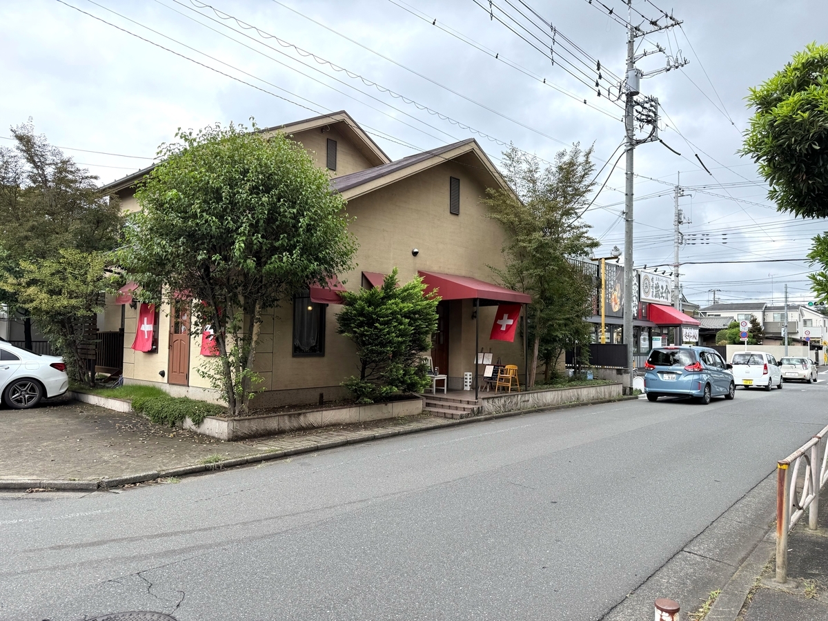 東大和市の住宅街に建つスイス家庭料理店ル・シャレーの外観。ベージュの壁に赤いひさし、窓にスイス国旗が掛かる一軒家