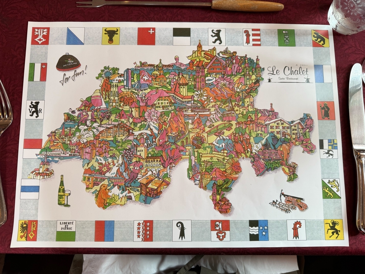 ル・シャレーのランチョンマット。中央にスイス全土のイラスト地図、周囲にスイス各州の紋章が並び、フォンデュ用の長い串が置かれている