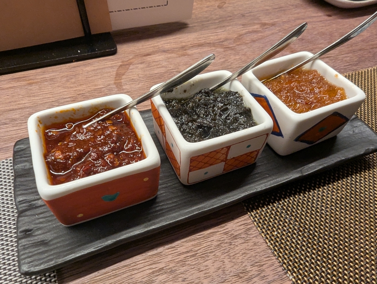 黒い板皿にのった3種の醤。赤い辛味の醤、黒い香港オリーブ醤、オレンジ色のXO醤がそれぞれ小さな角皿に入っている