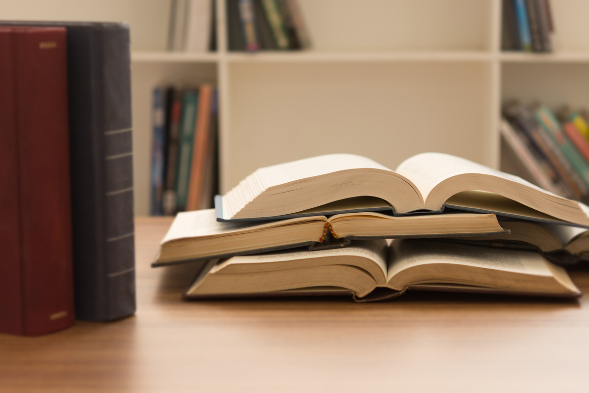 書斎や図書館のような本に囲まれた場所で、机に広げて積み重なっている本
