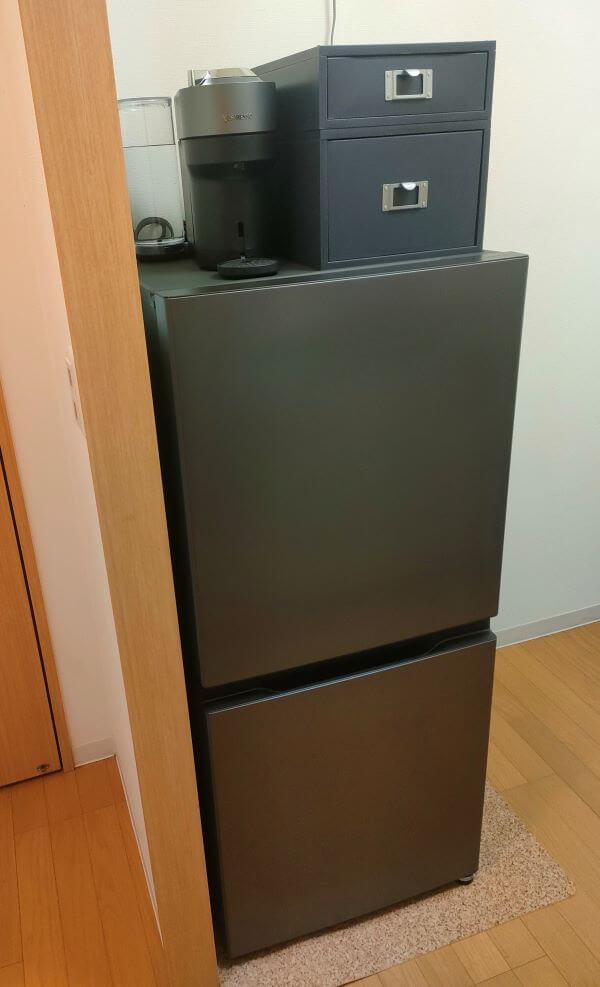 ダークシルバーのAQUA2ドア冷蔵庫の上に同色のコーヒーマシンと収納ケースを置いた状態