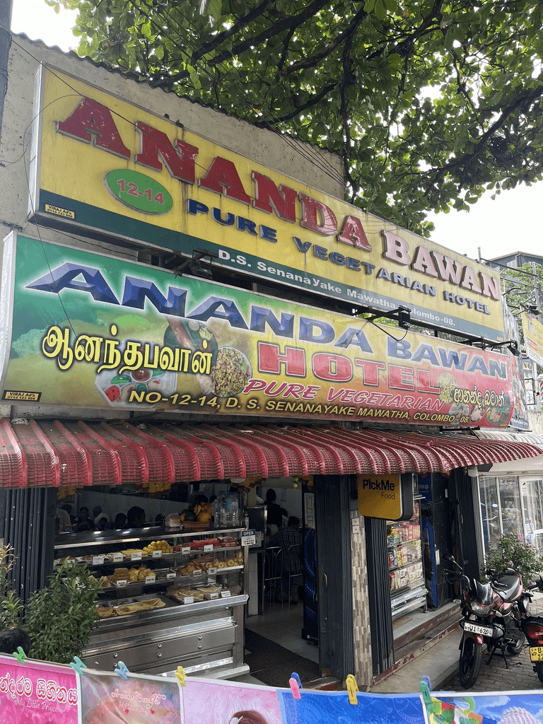 コロンボの人気ベジタリアンレストラン『Ananda Bawan』の外観。看板には英語・タミル語・シンハラ語で「Pure Vegetarian Hotel」と書かれており、入口にはスナックが並ぶ