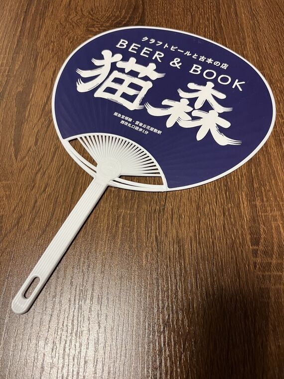 紺地に「BEER &amp; BOOK 猫森 クラフトビールと古本の店」と書かれたうちわの裏面