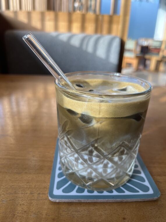 Grindのアイスほうじ茶ラテ。琥珀色の液体とガラスのストロー、青いコースター