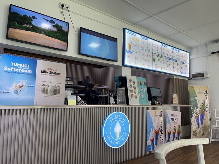 TUMUGIの店内カウンター。電光メニューボードにSOFTCREAM CONE、SOFTCREAM CUP、SHAKES、MILK DRINKS、JAPAN SELECTIONなどのカテゴリが並ぶ