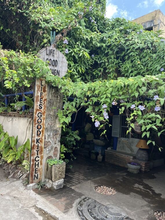 Life's Good Kitchenの入口。木の看板に店名、蔦と紫の花に囲まれている
