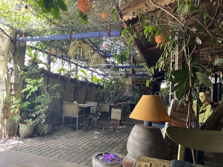 Life's Good Kitchenの屋外テラス席。植物と吊り飾りに覆われたパーゴラの下に木製のテーブルと椅子