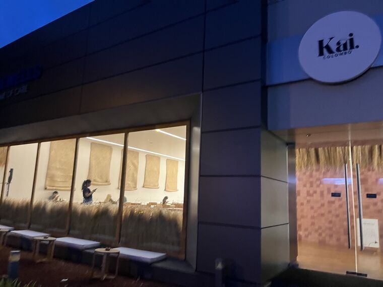夜のKai. CMBの外観。大きなガラス窓の内側に麦の造花が並び、店内で過ごす客が見える