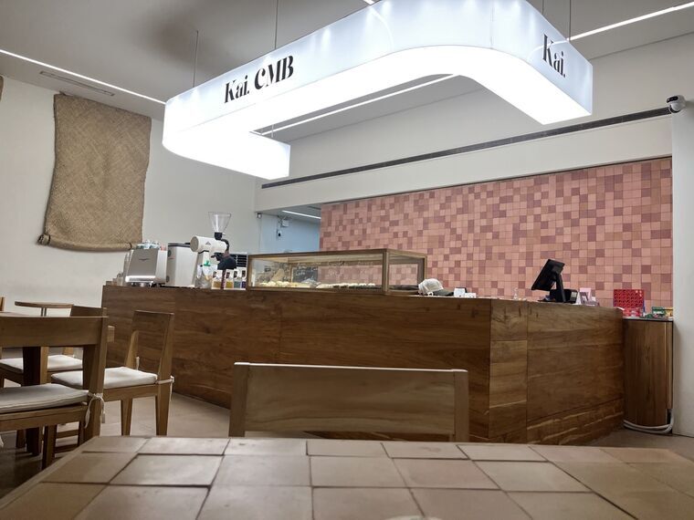Kai. CMBのカウンター。上部にKai. CMBと光る看板、奥はピンク系のタイル壁、エスプレッソマシンと焼き菓子のショーケース