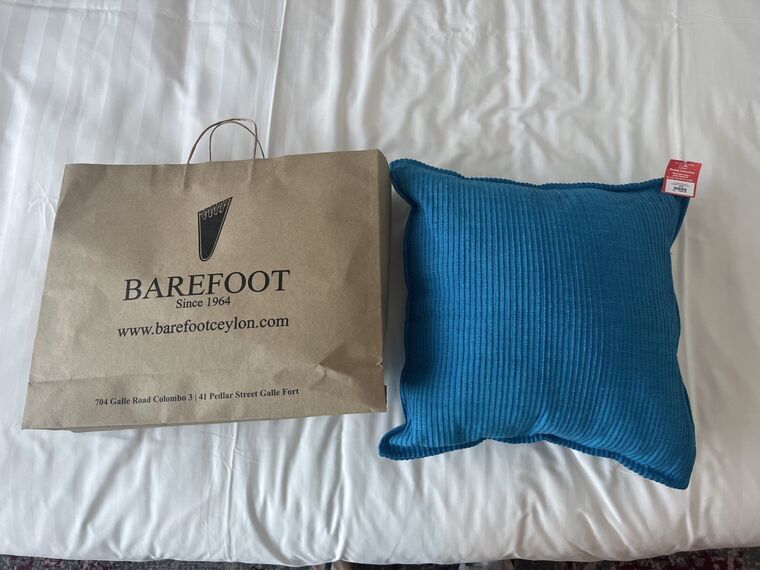 BAREFOOTの茶色い紙袋と、青いクッション。紙袋にBAREFOOT Since 1964 www.barefootceylon.comと印字されている