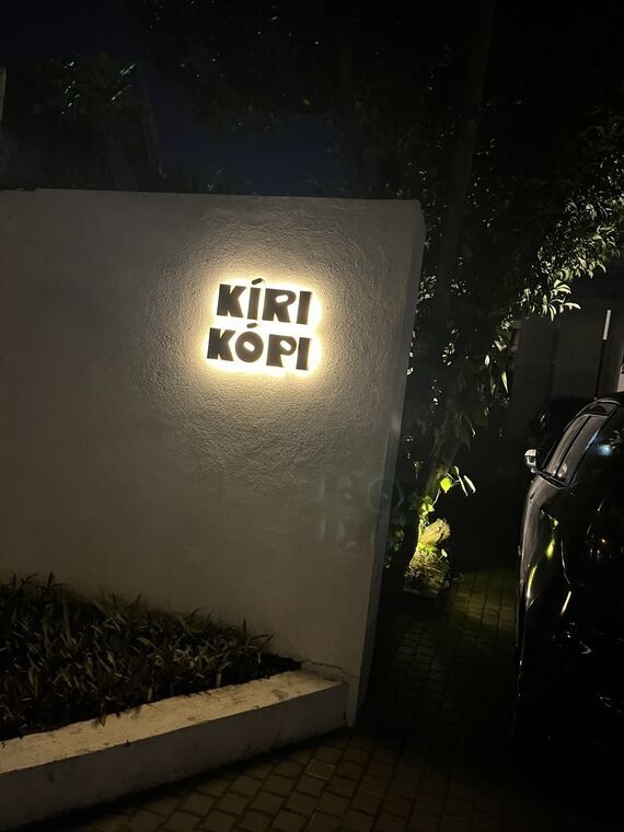 夜のKIRI KOPIの照明サイン。白壁に立体文字が浮かび、手前に植栽と駐車中の車がある
