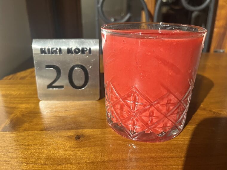 カットグラスに入った鮮やかな赤紫色のジュース。隣にKIRI KOPIと20が刻まれた金属製のテーブル番号札