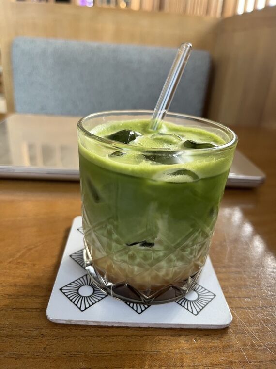 Grindのダーティーマッチャラテ。カットグラスに入った鮮やかな緑色のアイスラテ、ガラスストロー付き。グラスの下のほうが茶色くなっている