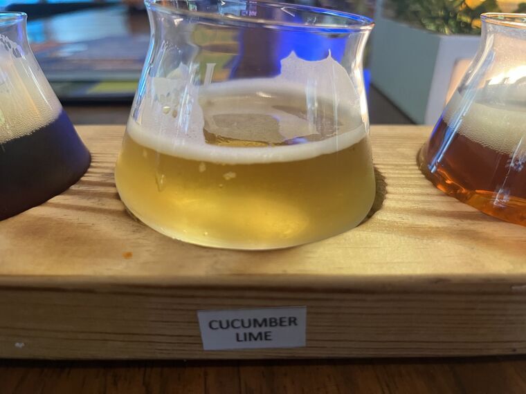 淡い黄色のビール。泡はやや少なめ。手前の木札にCUCUMBER LIME