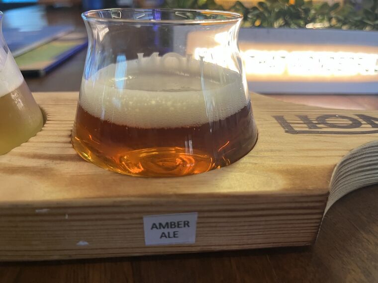 オレンジから琥珀色のビール。厚い白い泡。手前の木札にAMBER ALE