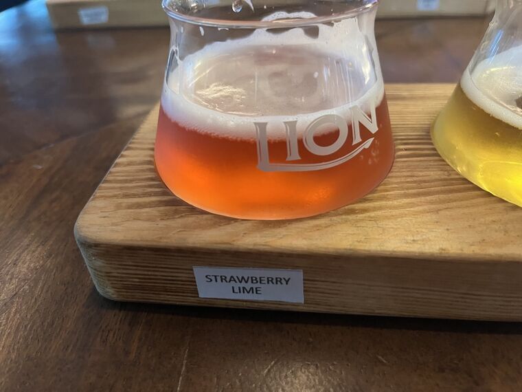 赤からオレンジがかったピンク色のビール。厚い白い泡。手前の木札にSTRAWBERRY LIME