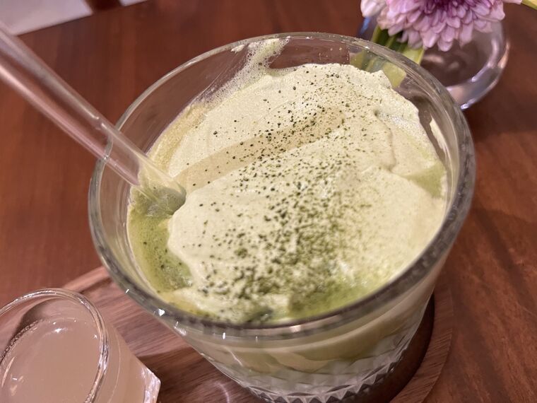 抹茶ラテの表面のクローズアップ。細かいミルクフォームの上に抹茶パウダーが振りかけられている。ガラスストローが挿さっている