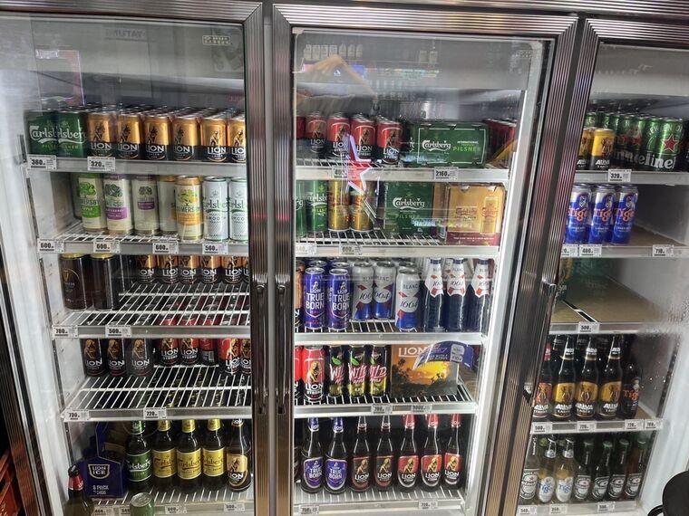 3扉のガラス冷蔵ショーケース。Carlsberg Pilsner 360、LION 320、Somersby各種600、Carlsberg Smooth 560などの値札が棚に並ぶ
