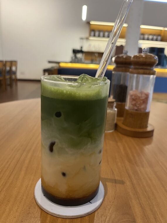 RADICLEのDirty Matcha Latte。縦長のグラスに濃い抹茶グリーン、白いミルク、茶色いエスプレッソの3層が上から順に重なっている。奥にバーカウンターと塩・胡椒のミル
