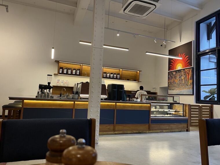 RADICLEのカウンター全景。紺と木目のカウンター、上部の棚にコーヒー豆のパッケージ、右手にケーキのショーケース、奥の壁に赤い太陽を描いた絵
