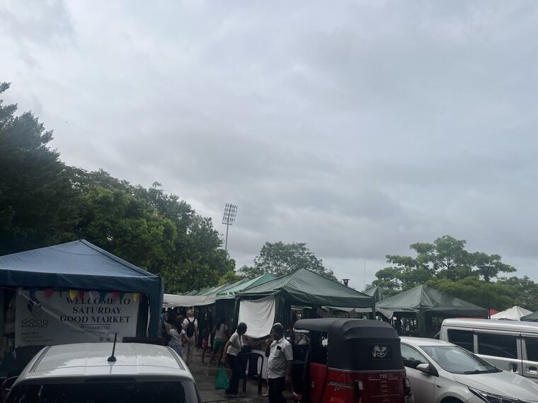 Saturday Good Marketの入口。青いテントにWELCOME TO SATURDAY GOOD MARKET、GOOD MARKETのロゴ。奥に緑のテントが連なり、手前にトゥクトゥクと車が停まっている