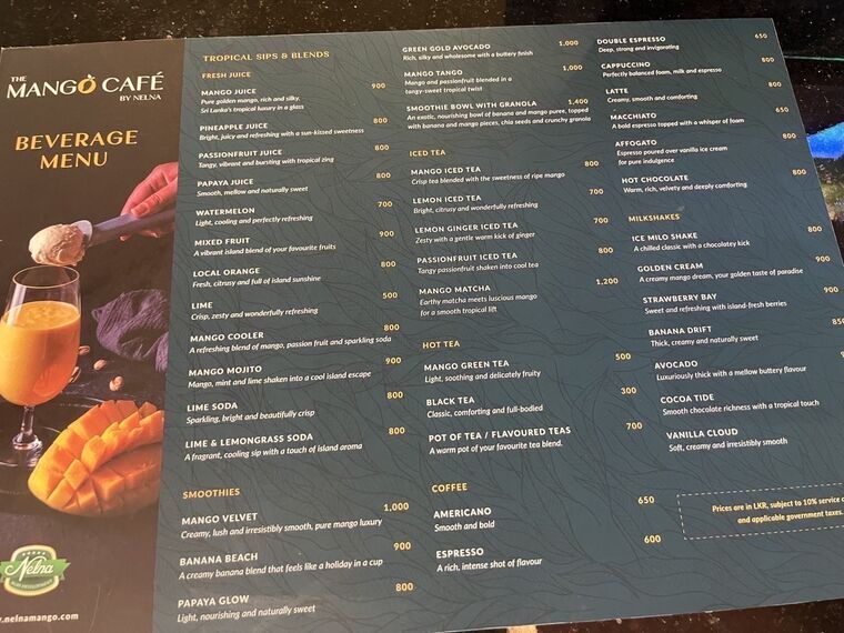 The Mango Cafe by NelnaのBEVERAGE MENU。深緑の紙面にTROPICAL SIPS & BLENDS、SMOOTHIES、ICED TEA、HOT TEA、COFFEE、MILKSHAKESの各セクションと価格が金色で並ぶ