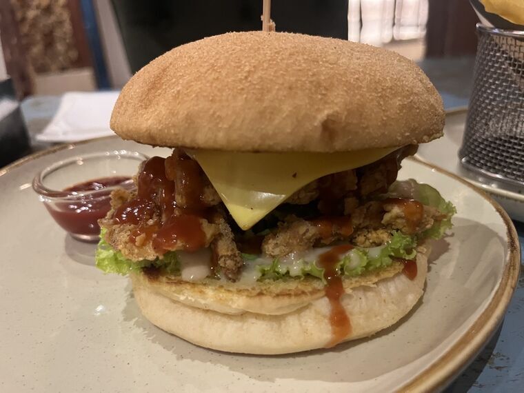 バーガーのクローズアップ。大きなバンズの間に衣をつけて揚げたマッシュルーム、レタス、チーズ1枚、赤いソース。具の層がバンズに対して薄い