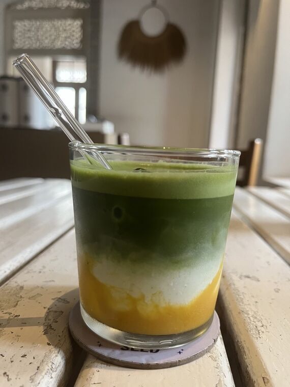 Seed CafeのMatcha Peach & Mango。グラスの上部が明るい緑の抹茶、中央が白いミルク、底がオレンジ色のピーチとマンゴー。ガラスストローが差してある
