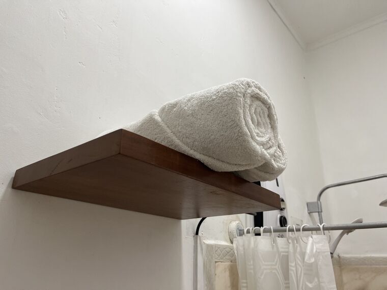 シャワーとトイレの空間にある木の棚。丸めた白いバスタオルが載っている。右にシャワーカーテンとカーテンレール