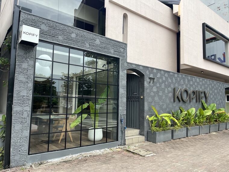 Kopify Colomboの外観。グレーの石壁に立体のKOPIFYロゴと番地77、黒枠の格子窓