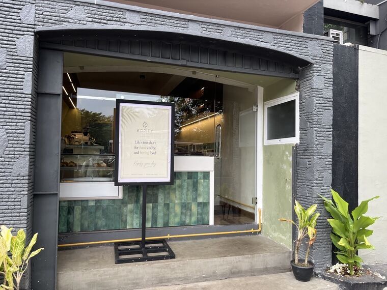 Kopifyの入口。Life's too short for basic coffee and boring food.と書かれたスタンド看板、奥にエスプレッソマシンとペストリーのショーケース