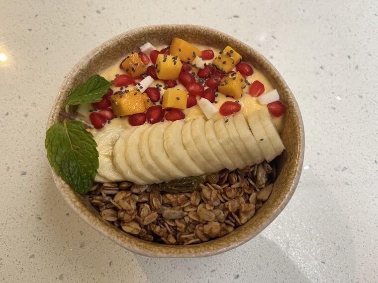 Tropical Sunrise Bowlを真上から。左半分がグラノーラ、右半分がマンゴーのソース、中央にスライスしたバナナ、上にマンゴーの角切りとザクロとココナッツとチアシード