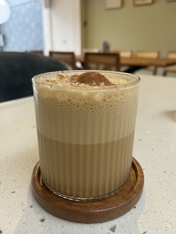 Salted Kithul Latte。木のコースターに載ったグラス、上半分が泡で下が二層に分かれ、中央にシナモンパウダーが山になっている