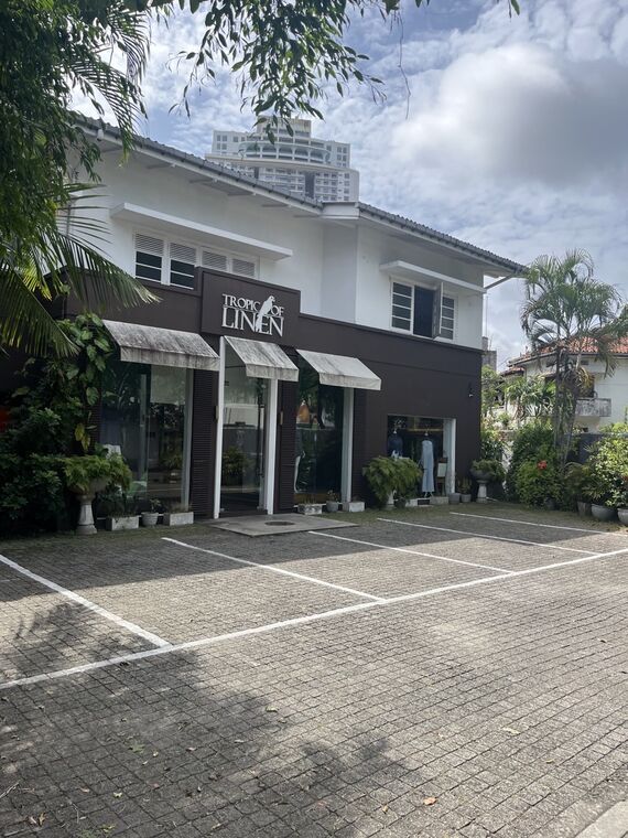 Tropic of Linenの外観。白い壁に濃い茶色の庇が付いた2階建て、庇に店名の表記、手前に駐車スペース