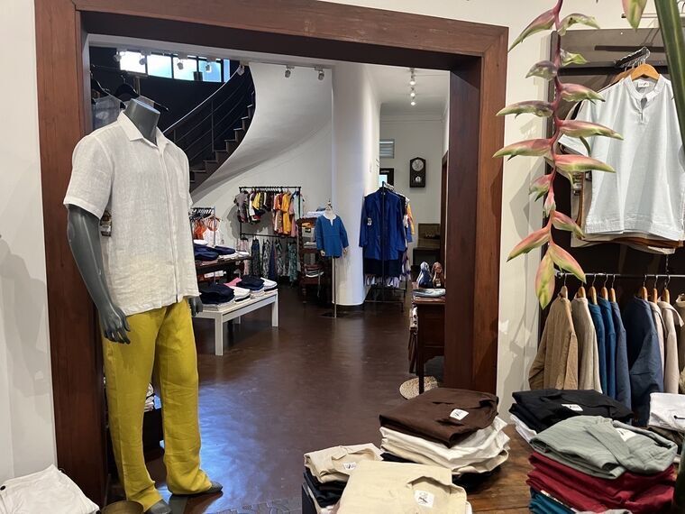 入口から見た店内。白いリネンシャツと黄色いズボンのマネキン、奥にカーブした階段とレディースのフロア