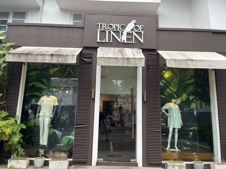Tropic of Linenのファサード。庇に店名の刺繍風の表記、白い柱と黒い格子窓、看板に鳥のロゴ