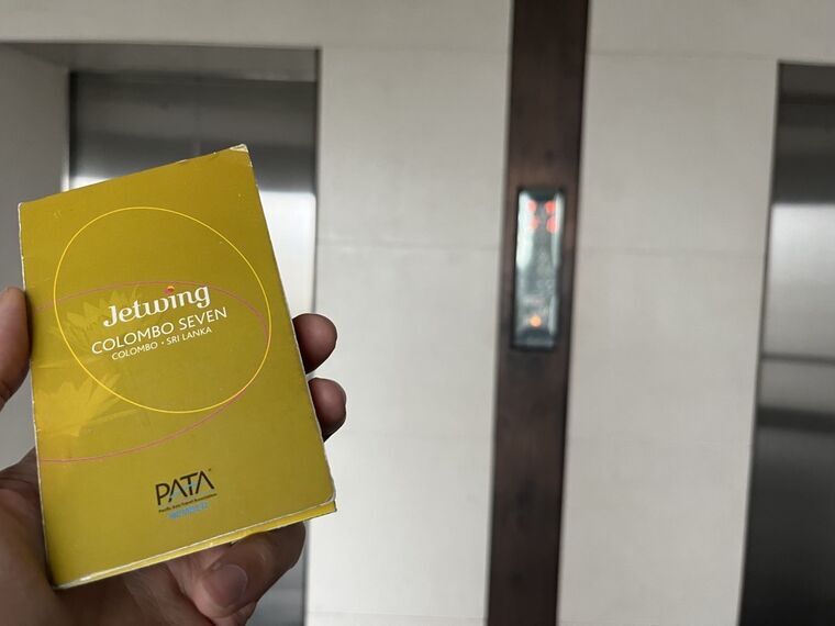 黄色いルームカードのケースを手に持った写真。Jetwing COLOMBO SEVEN、COLOMBO・SRI LANKA、PATA MEMBERの表記。背景にエレベーター2基